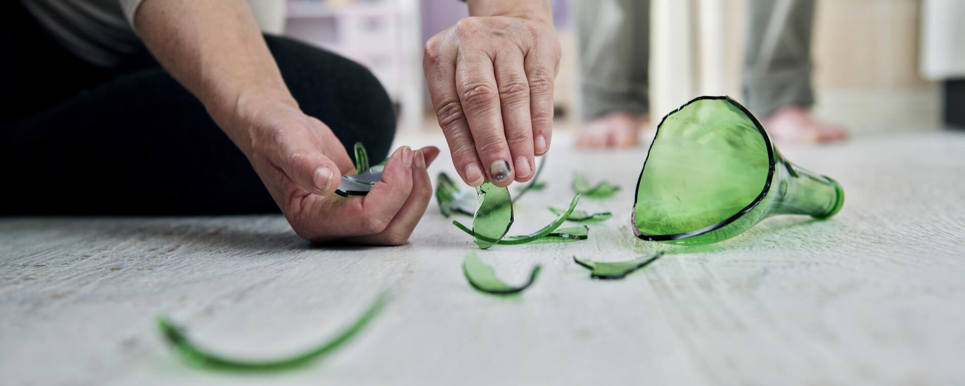 woman picking up the pieces of broken alcohol bottle
