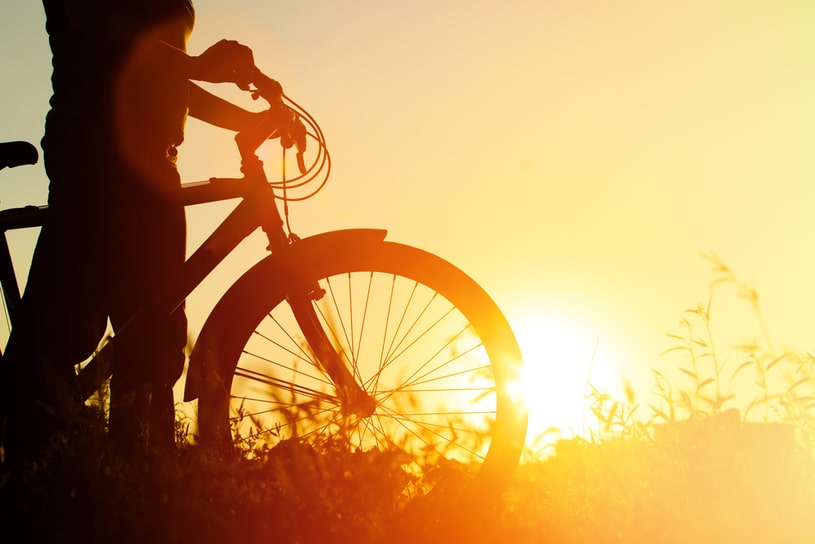 A man with a bicycle during sunset.
