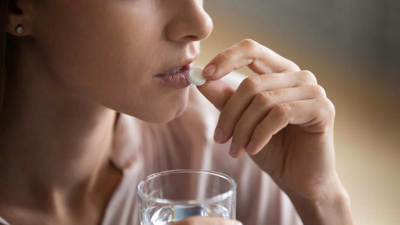 Woman with a glass of water in her hand takes an Ambien pill.