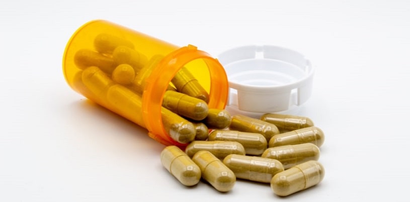 Green capsules of Kratom powder spilling out of an orange pill bottle.