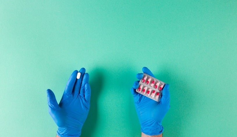 Hands in gloves holding Tramadol and Norco pills on green background.