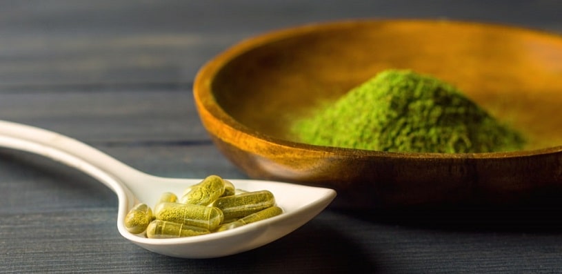 Kratom capsules in ceramic spoon on table.