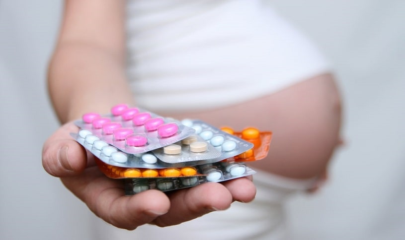 Pregnant woman holding pill blisters.