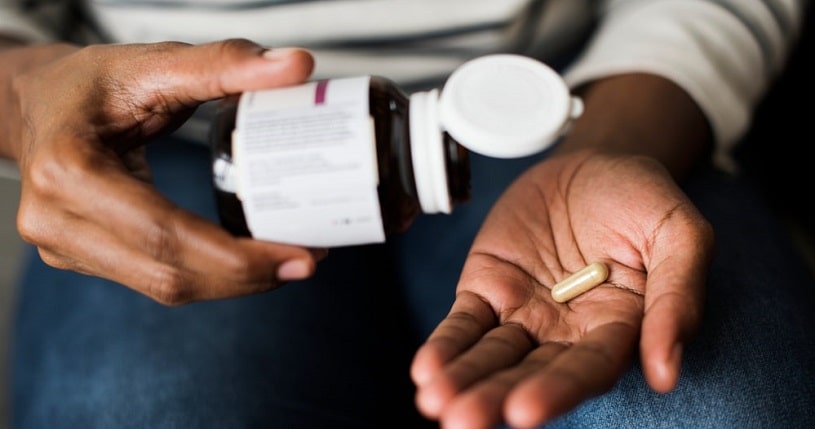 Woman taking Kratom capsules from the bottle.