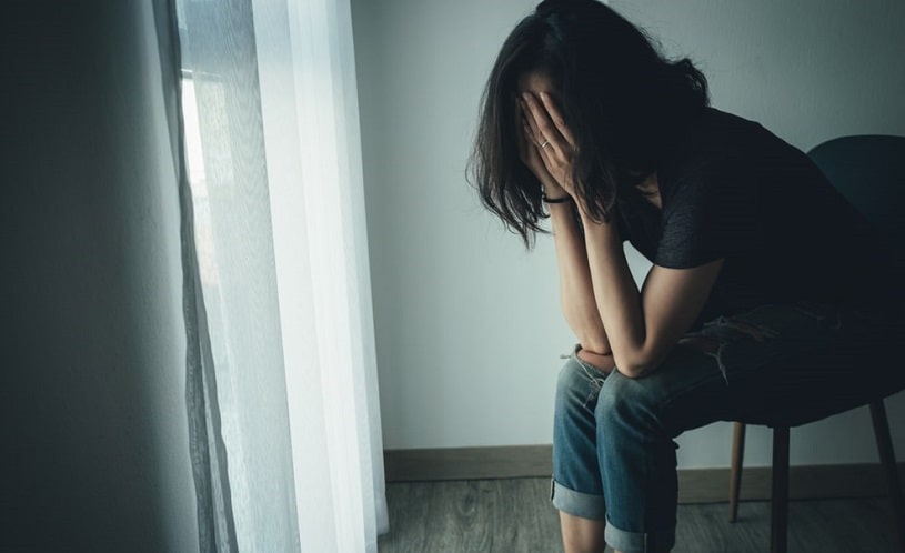 Young depressed woman sitting on the chair covering her face.