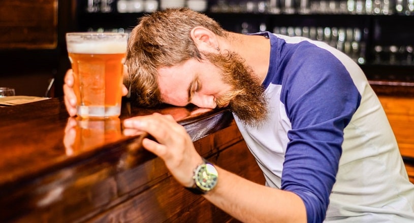 Drunk man sleeps and holds a glass of beer.