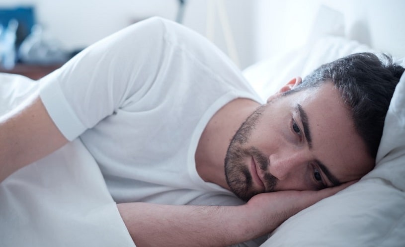 Depressed man experiencing pain lying in bed.