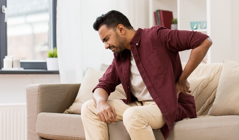 Man experiencing pain sitting on the couch at home.