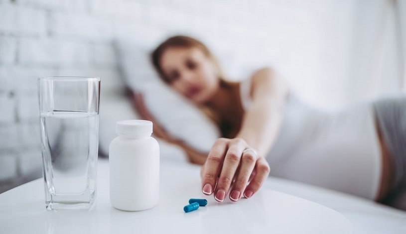 Sick woman lying in bed taking pills.