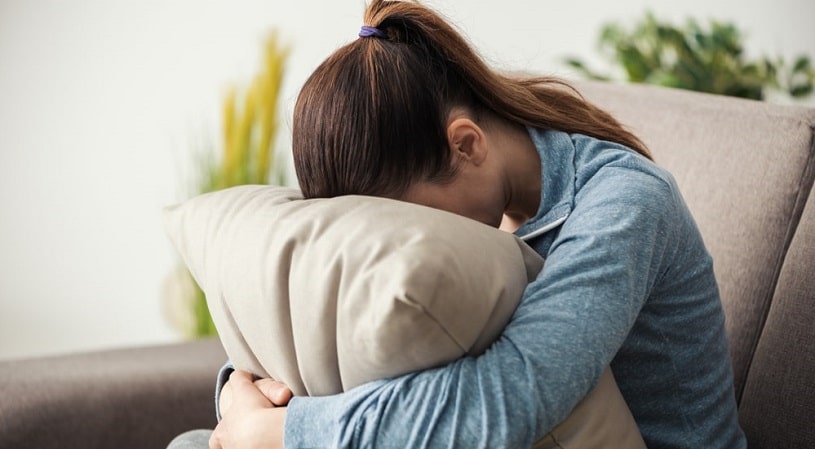 Depressed woman holding a pillow hiding her face.