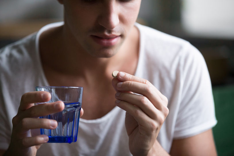 A man holds a glass of water in one hand and Demerol pill in another.
