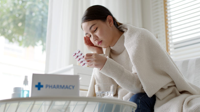 A woman is sitting in the sofa and experiencing a headache because of Fiorinal side effects.
