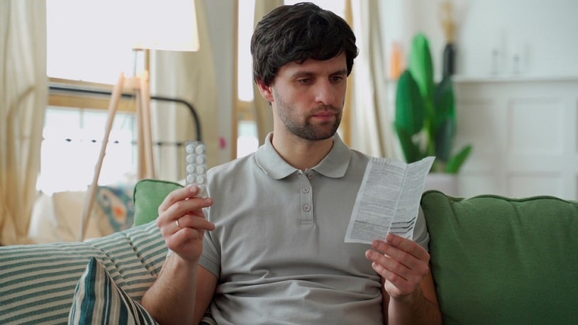 Man with medications reading instruction for Baclofen use.
