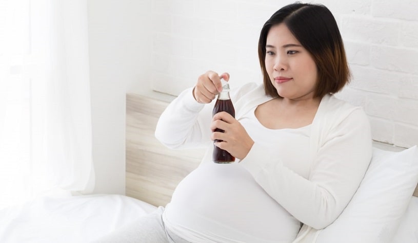 Pregnant woman on bed drinking coke with caffeine.
