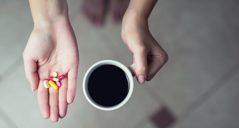 Woman holding coffee cup and caffeine supplements in hand.