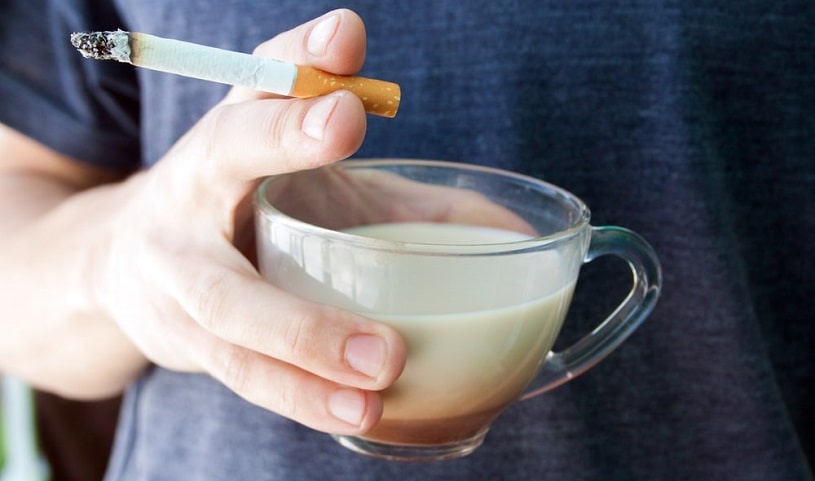 Man holding a cigarette and a cup of coffee.
