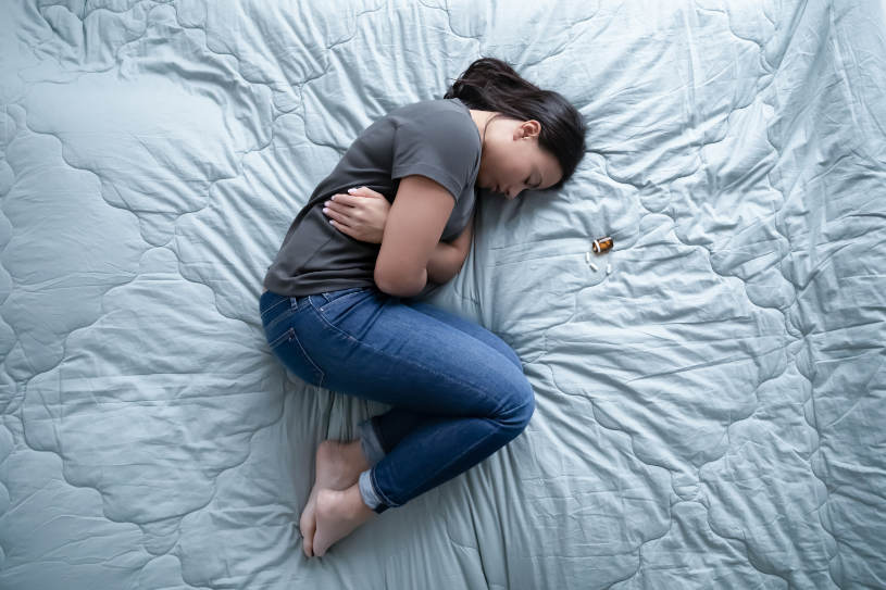 Deeply unhappy depressed african mixed race young woman lying on bed near bottle and heap of pills.