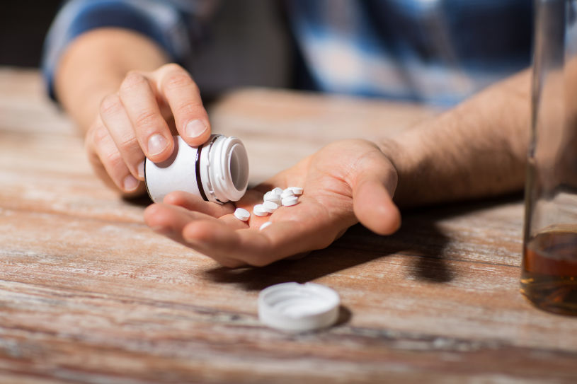 Unhappy drunk man with bottle of alcohol and pills.