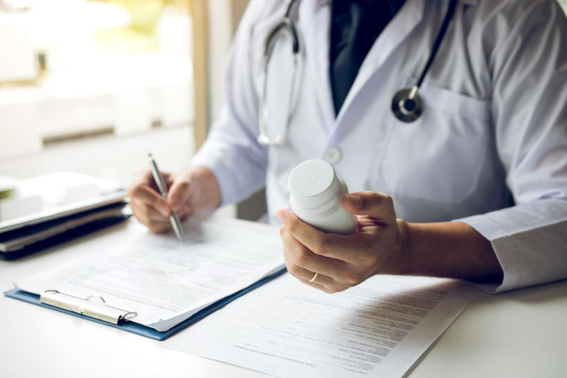 A doctor man holding a pill bottle and writing while talking with a patient and reviewing his medication at office room.