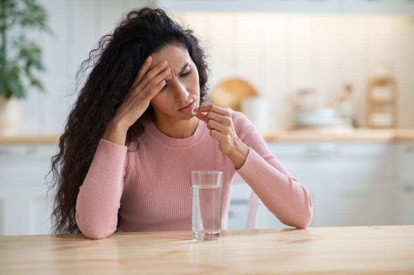 A woman with a glass of water and a pill in her hand.