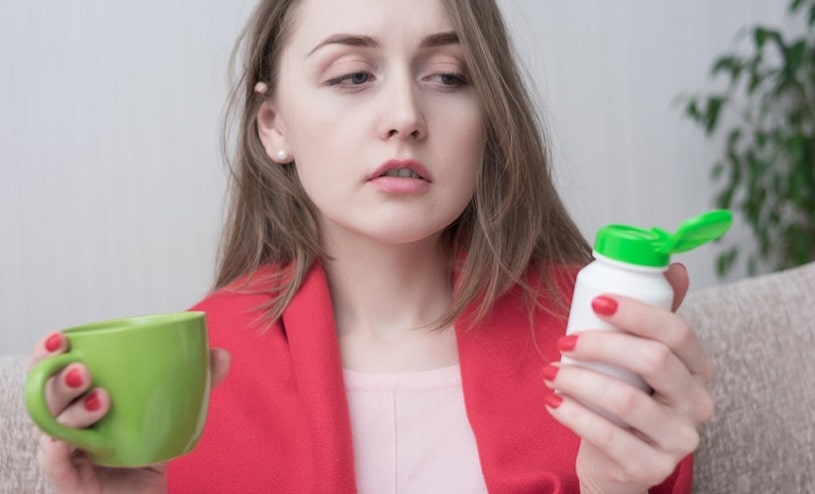 Woman with a cup and pills in hands thinking about stopping Ritalin use.