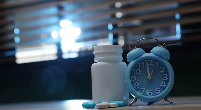 Alarm clock and pills on the table indoors.