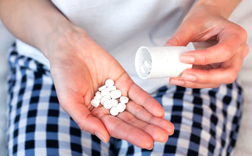 Young woman holds pills and a pill bottle in her hands.