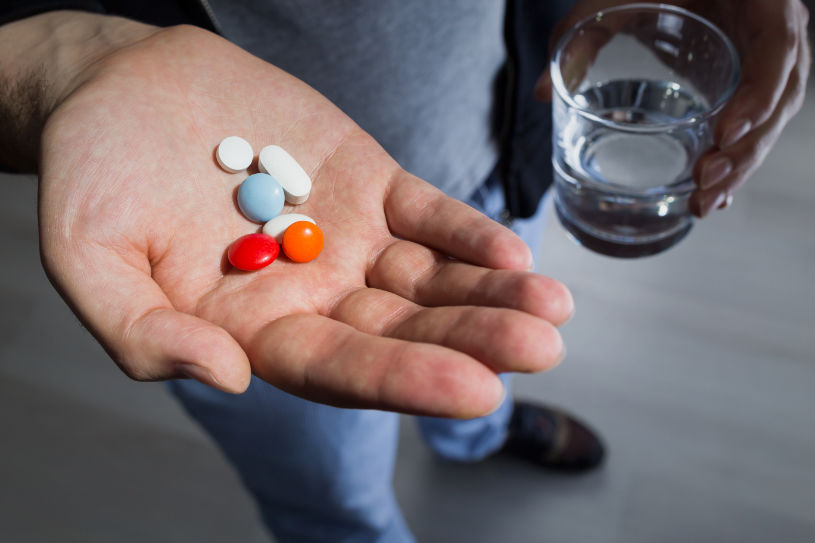 A man holds pills and a glass of water.