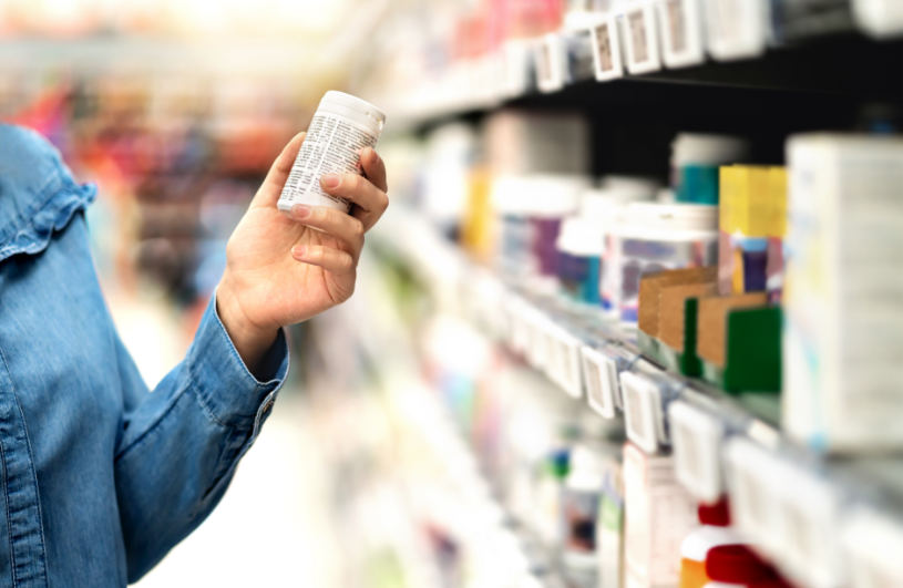 A woman holds a bottle of pills in the pharmacy.