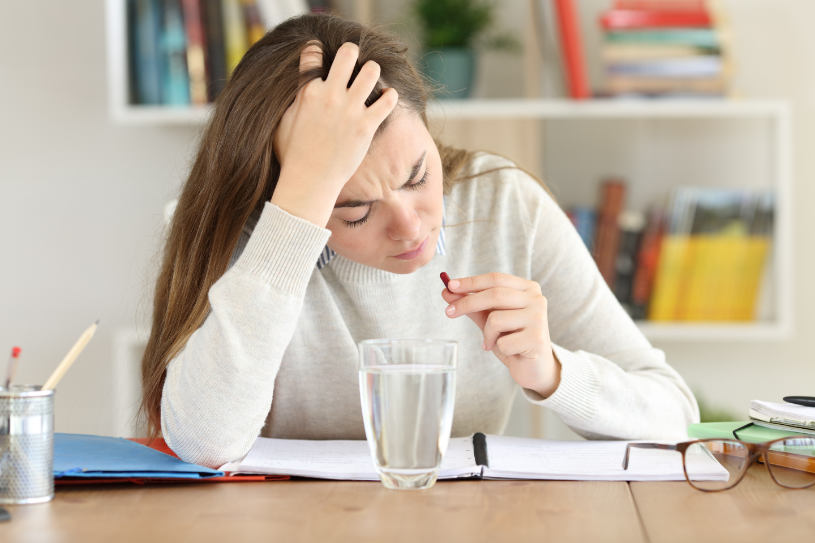 A woman with a headache drinks a pill.