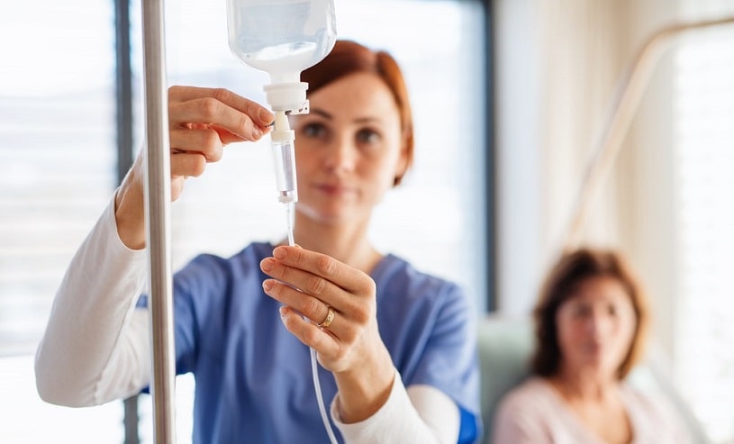 A nurse with IV drip and patient in hospital bed.
