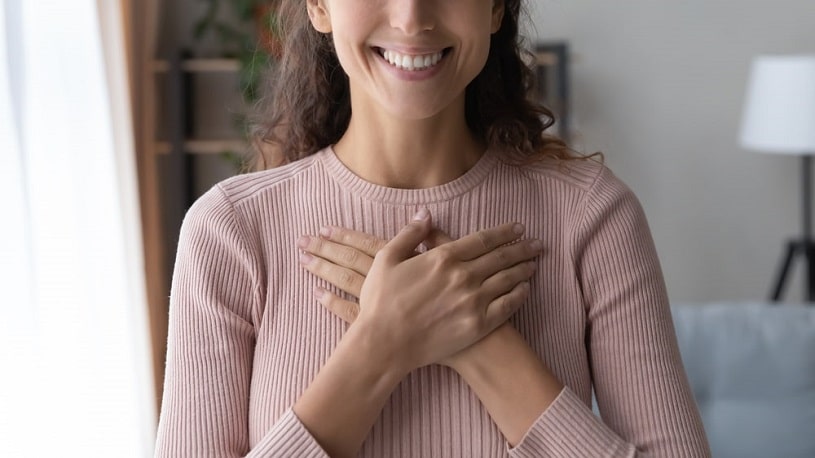 Calm and delighted woman holding folded hands on chest.