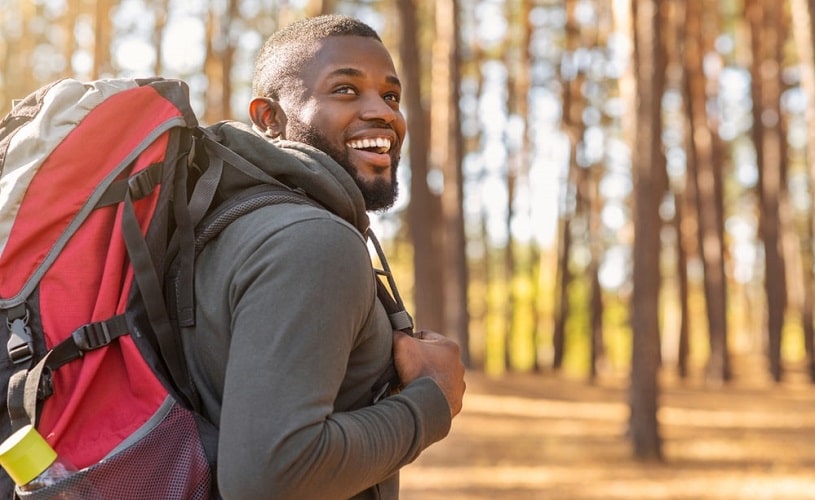Man with backpack smiling during adventure therapy hiking.
