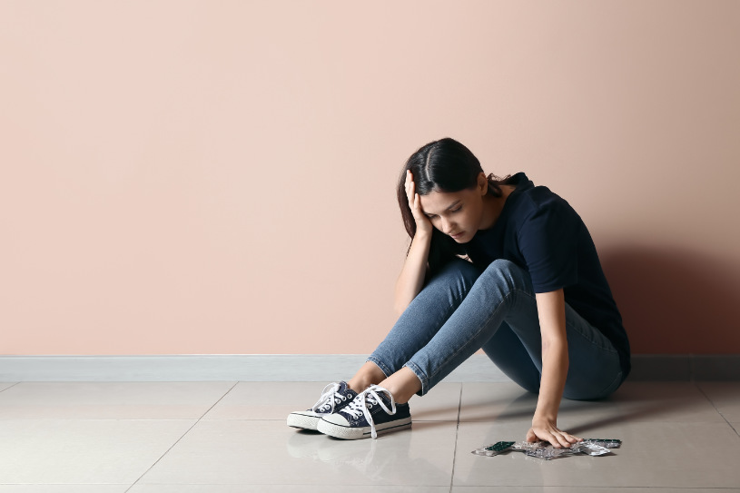 A girl is sitting on the ground and watching at Trazodone pills.