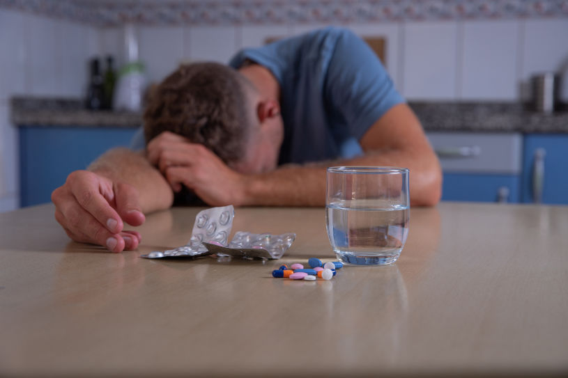 A man in pain and different pills lie near him.