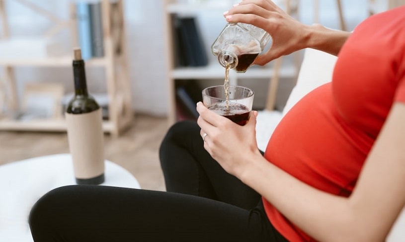 Pregnant woman at home drinking alcohol.