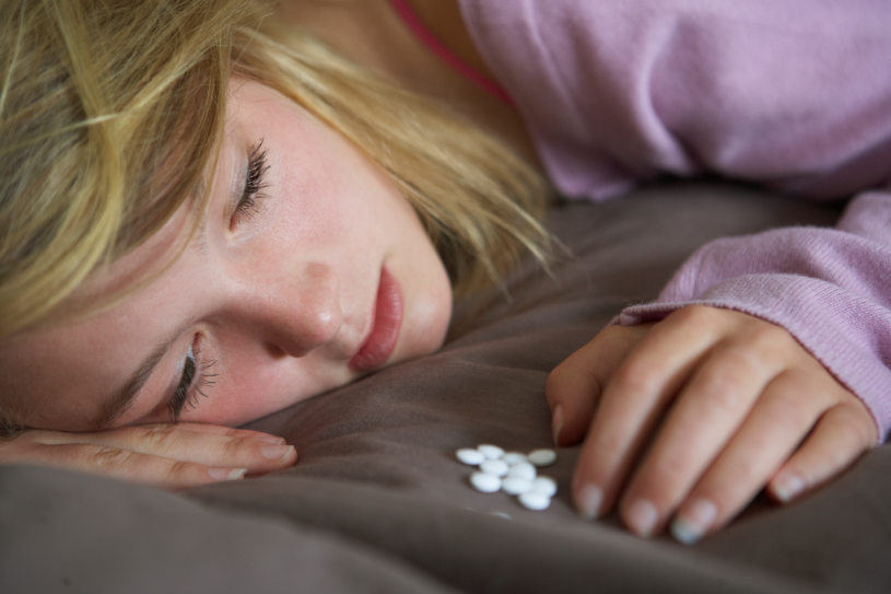 A depressed woman lies in bed and looks at Trazodone pills.