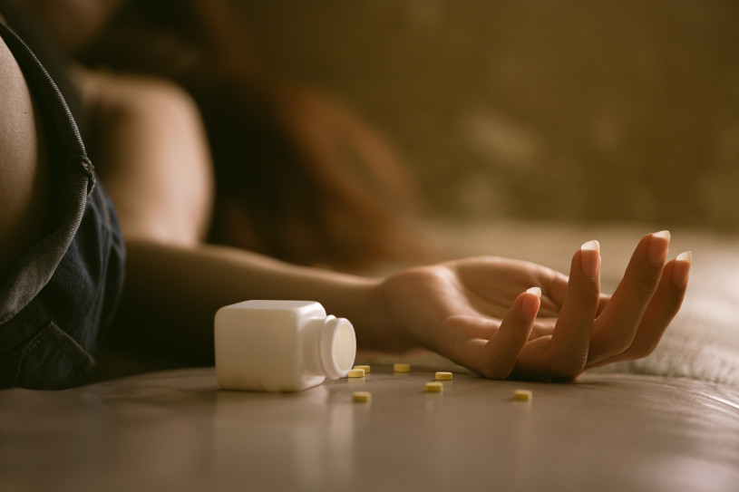 A woman lying in bed and pills dropะทed near her hand.