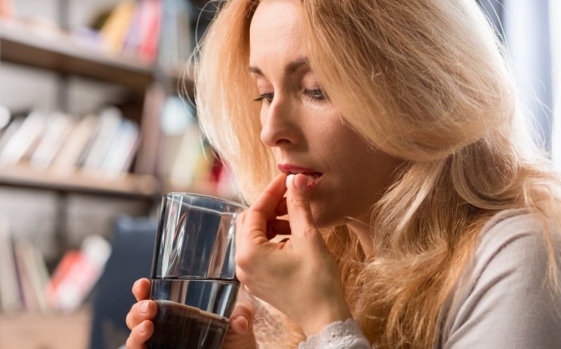 Woman taking a pill with a glass of water.