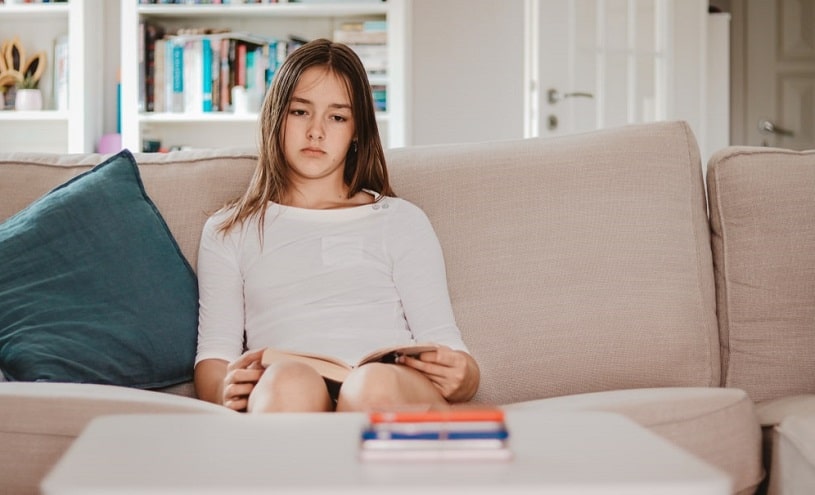 Teenage girl sitting at home with a sad expression.