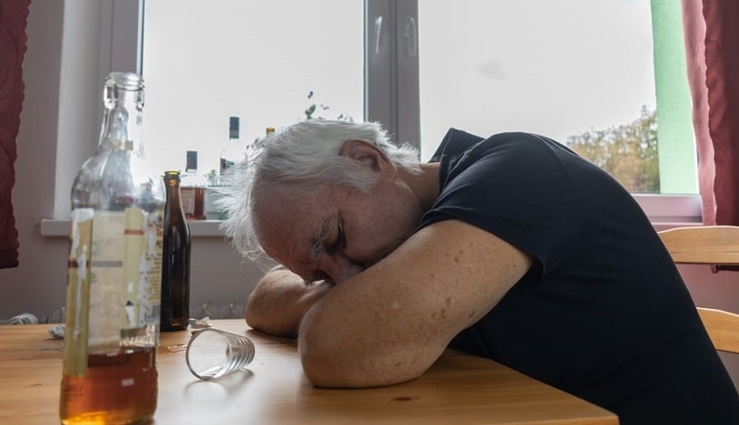 Old senior male sleeping next to table.
