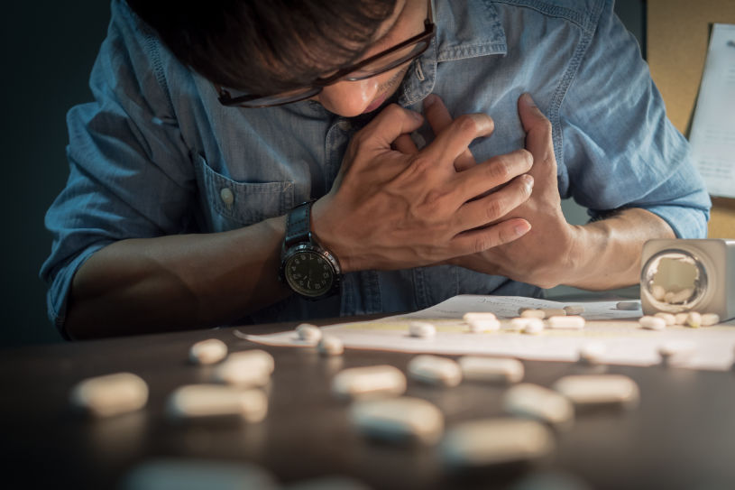Some pills on the table and a man having heart attack on the background.