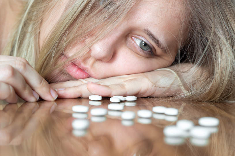 A depressed woman look at antidepressant pills on the table.