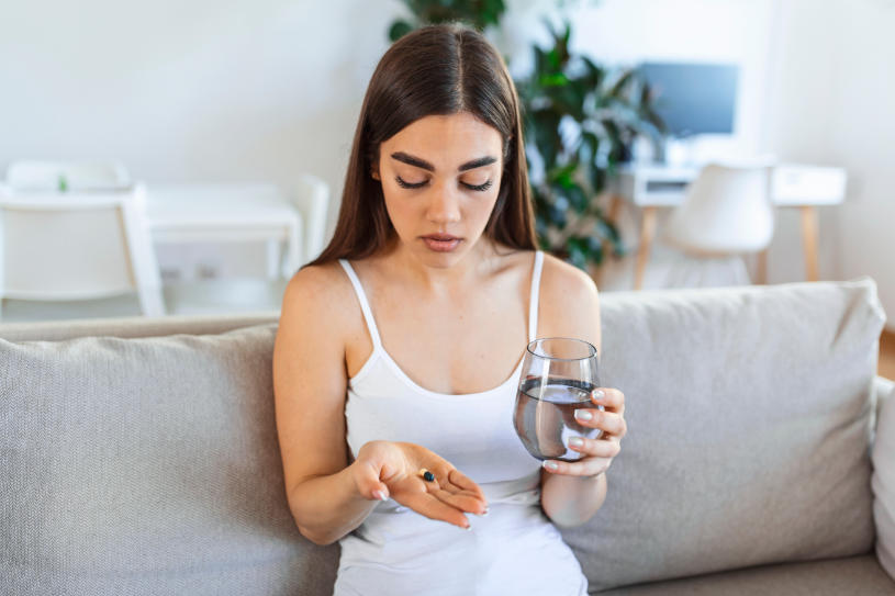 A girl holds a glass of water and looks at a pill.
