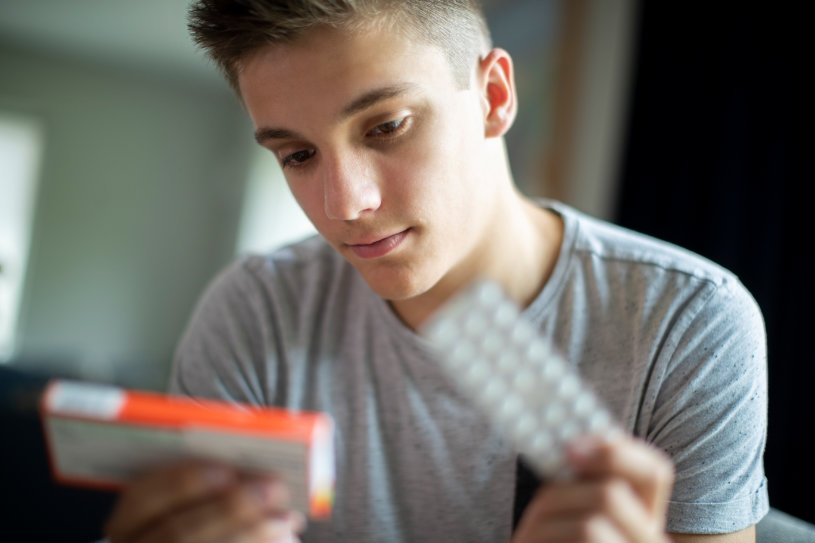 A man holding some pills and reading the drug instruction for use.