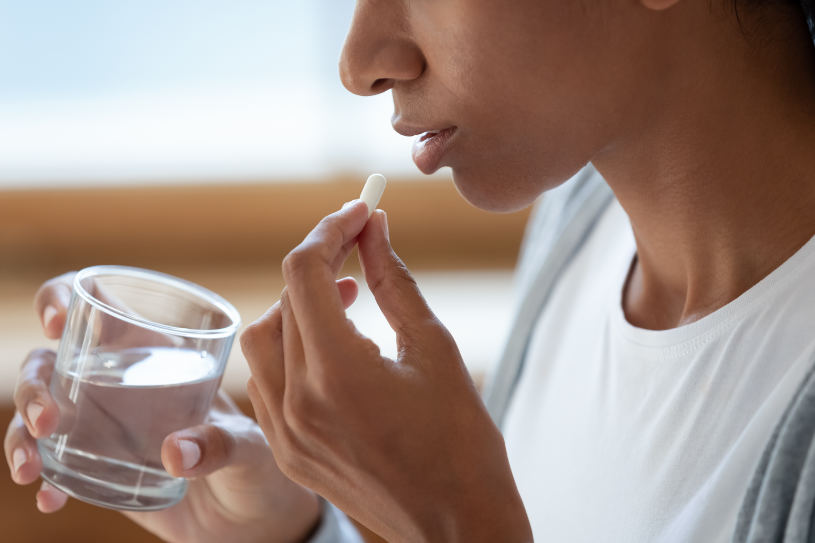 A woman holds a glass of water and drinks a pill.