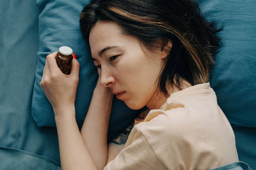 A woman lies in bed and holds a bottle of pills.
